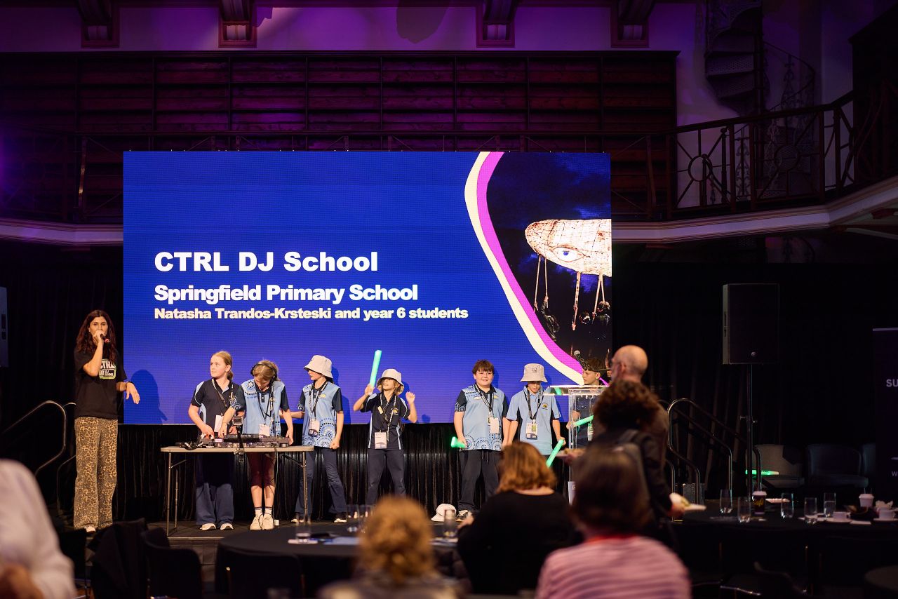 Miss Tash speaking on stage beside CTRL DJ School students
